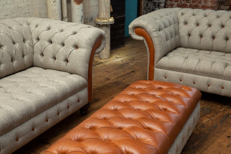 May include: A brown leather tufted ottoman with a gray tweed sofa in the background.