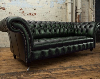 May include: A dark green Chesterfield sofa with button tufting and rolled arms. The leather sofa has a classic design with nailhead trim along the arms and base. The sofa sits on short, dark wooden legs with metal casters.