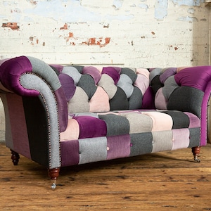 May include: A patchwork sofa with a tufted back and arms. The sofa is upholstered in a variety of fabrics, including velvet, tweed, and cotton. The sofa is a light grey, pink, and purple colour.