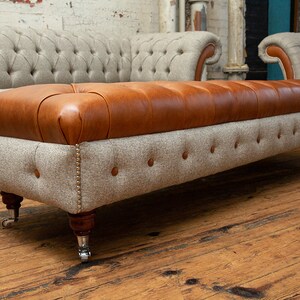 May include: A brown leather and gray tweed ottoman with tufted upholstery and wooden legs with silver casters.