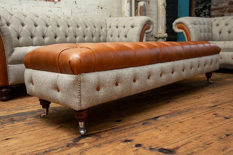 May include: A brown leather and gray tweed ottoman with tufted upholstery and wooden legs with silver casters.