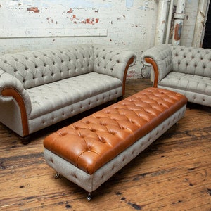 May include: A set of three tufted furniture pieces in a living room setting. A light gray sofa with brown trim, a matching armchair, and a brown leather tufted ottoman with a gray base.