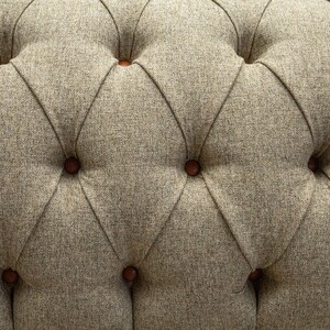 May include: Close-up of a tufted fabric upholstery with a diamond pattern and brown buttons. The fabric has a subtle texture and a neutral beige color.