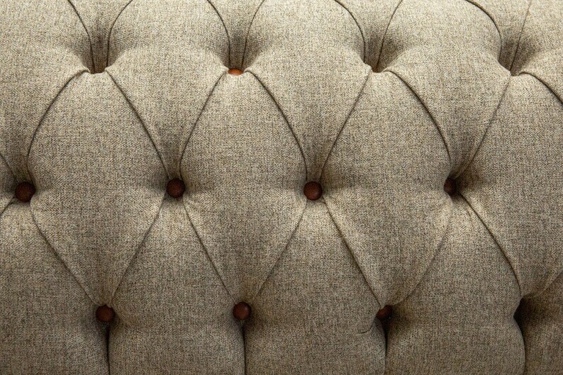 May include: Close-up of a tufted fabric upholstery with a diamond pattern and brown buttons. The fabric has a subtle texture and a neutral beige color.