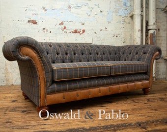 May include: A gray and brown plaid sofa with a tufted back and leather trim. The sofa has a classic design and is upholstered in a durable fabric. The sofa is sitting on a wooden floor.