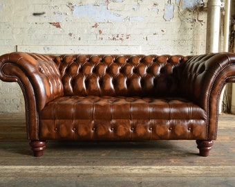 May include: A brown leather chesterfield sofa with button tufting and wooden legs.