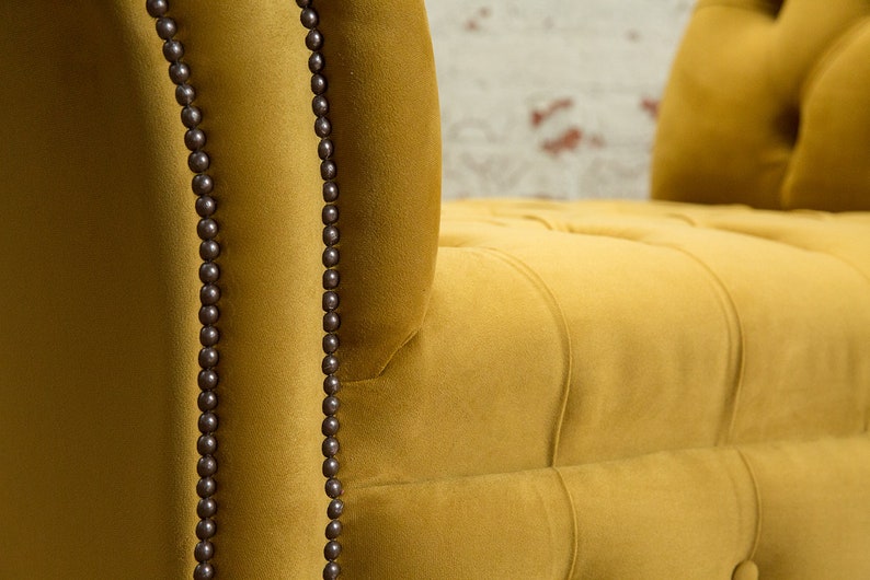 Puede incluir: Primer plano de un sill&oacute;n de terciopelo amarillo mostaza con tapicer&iacute;a capiton&eacute; y ribetes de cuentas marrones oscuras.