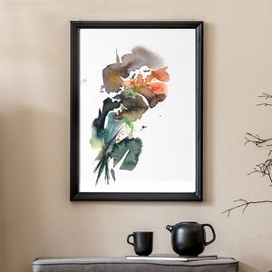 May include: A framed abstract watercolor painting featuring fluid washes of orange, brown, green, and black ink on a white background, displayed in a thin black frame hanging on a wall above a wooden bench with two drawers.