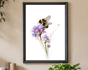 Può includere: Una stampa ad acquerello incorniciata con un'ape che svolazza sopra fiori viola e blu. L'opera d'arte è ambientata su uno sfondo bianco, incorniciata in nero e esposta in una stanza con piante e oggetti decorativi.