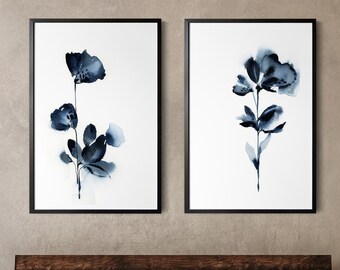 May include: Two framed watercolor floral prints. Each features a dark blue flower with leaves against a white background. The frames are black. The prints are displayed above a wooden bench with gray cushions and pillows.