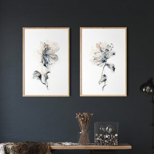 Puede incluir: Dos impresiones enmarcadas de acuarela floral con marcos de madera clara cuelgan de una pared azul oscuro. La obra de arte presenta flores abstractas en tonos de azul, beige y gris. Debajo de las obras de arte hay un banco de madera con una manta de piel y objetos decorativos.