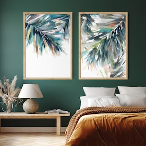 Puede incluir: Dos pinturas de acuarela enmarcadas de palmas abstractas en tonos turquesa, azul y marr&oacute;n. La obra de arte se exhibe en una pared verde oscuro sobre una cama con una manta color mostaza. Los marcos son de madera clara.