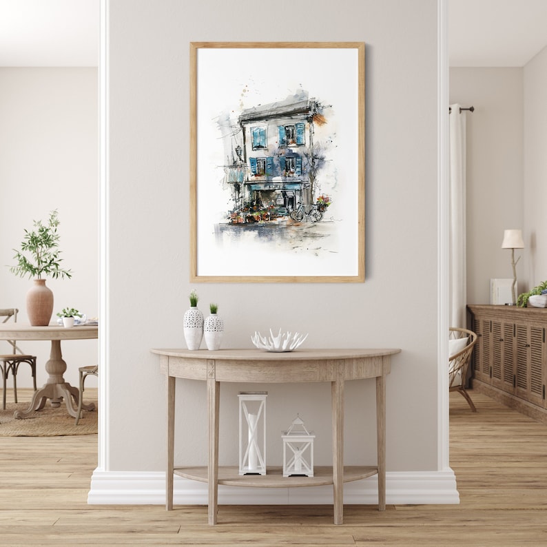 May include: Watercolour print of a European building with blue shutters and a flower shop. The artwork is framed in a light wood frame and hangs on a neutral wall. A bicycle is parked outside the shop.