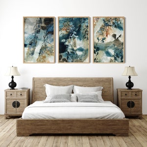 K&ouml;nnte beinhalten: Drei gerahmte Aquarelldrucke mit abstrakten botanischen Designs in Blau-, Braun- und Wei&szlig;t&ouml;nen. Das Kunstwerk h&auml;ngt &uuml;ber einem Holzbett mit passenden Nachttischen und Lampen.