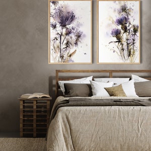 May include: Two framed watercolor paintings of purple thistle flowers. The artwork features a soft, blurred style with shades of purple, brown, and green. The paintings are displayed above a bed with a wooden frame and neutral-toned bedding.