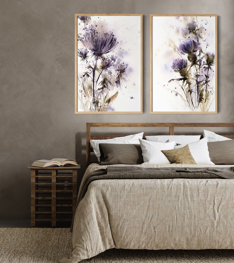May include: Two framed watercolor paintings of purple thistle flowers. The artwork features a soft, blurred style with shades of purple, brown, and green. The paintings are displayed above a bed with a wooden frame and neutral-toned bedding.