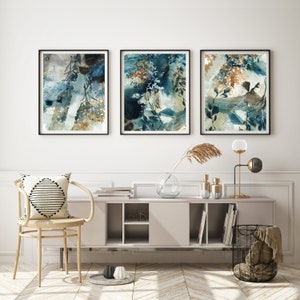 K&ouml;nnte beinhalten: Drei gerahmte abstrakte Aquarellmalereien in Blau-, T&uuml;rkis- und Braunt&ouml;nen. Das Kunstwerk zeigt botanische Elemente und wird &uuml;ber einer modernen Konsole mit dekorativen Gegenst&auml;nden ausgestellt.