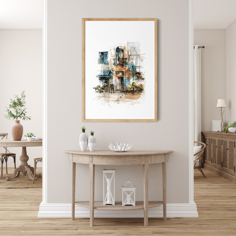 Op de afbeelding: Een ingelijste aquarelprint van een Europees gebouw met een bruine houten lijst. Het kunstwerk toont een gebouw met een blauwe luifel, luiken en bloemen. De print wordt weergegeven op een lichtgekleurde muur boven een houten console.