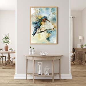 May include: Watercolor painting of a bird perched on a branch, framed in light wood. The bird features blue, green, and brown hues, set against a soft, abstract background of blues and yellows. The artwork is displayed in a well-lit interior setting.