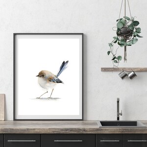 Puede incluir: Una impresi&oacute;n en acuarela enmarcada de un p&aacute;jaro peque&ntilde;o con cabeza marr&oacute;n, cuerpo blanco y plumas de cola azules. El p&aacute;jaro est&aacute; sobre un fondo blanco. El marco es negro. La impresi&oacute;n se exhibe sobre una encimera de madera.