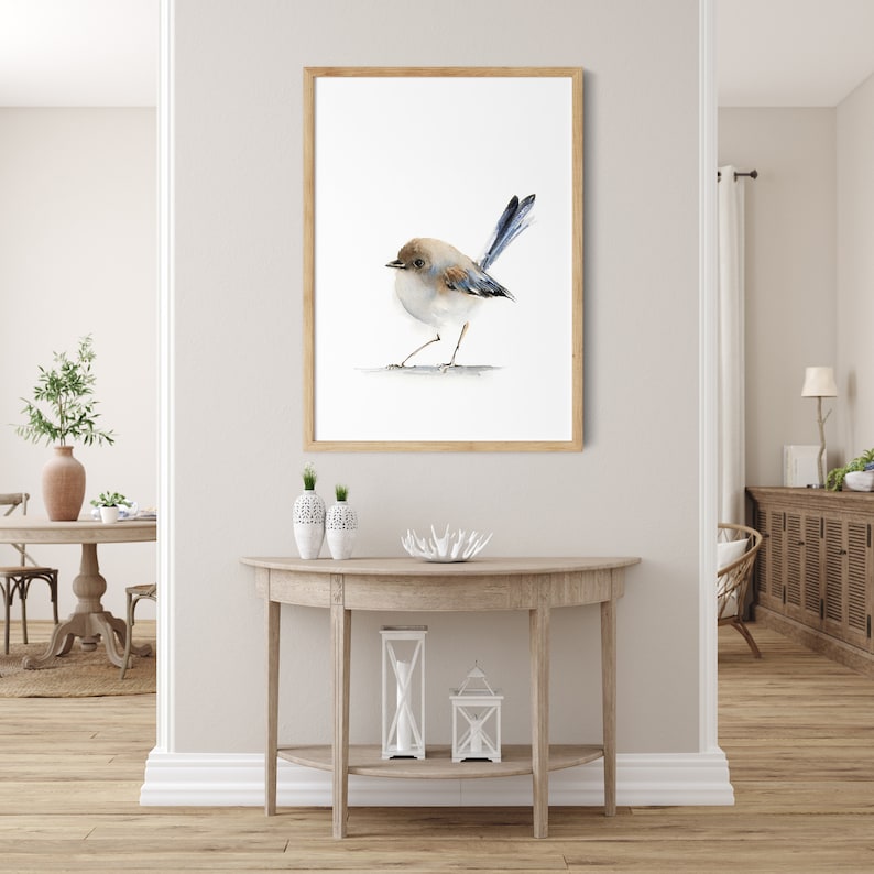 Puede incluir: Impresi&oacute;n en acuarela enmarcada de un p&aacute;jaro peque&ntilde;o. El p&aacute;jaro tiene la cabeza marr&oacute;n, el pecho blanco y las plumas de la cola azules. Est&aacute; sobre una l&iacute;nea fina sobre un fondo blanco. El marco es de madera marr&oacute;n claro.
