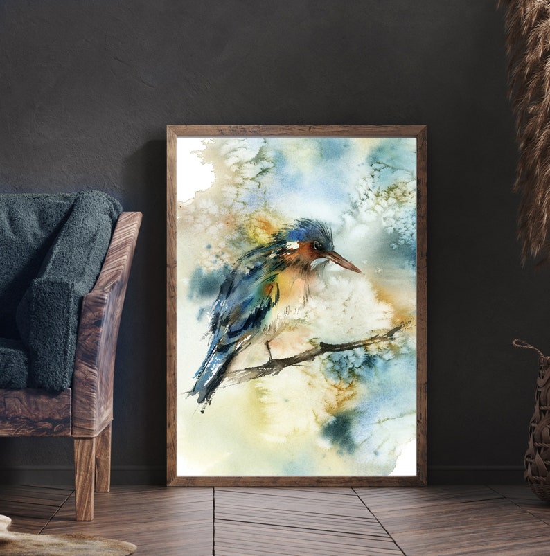 May include: Watercolor painting of a bird perched on a branch, set in a wooden frame. The bird features blue, orange, and yellow hues. The background has soft watercolor washes of blue, yellow, and brown.