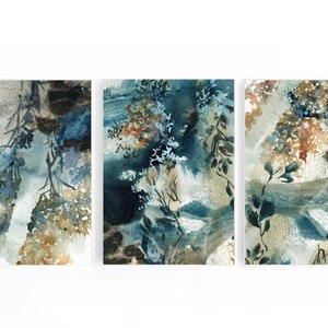 K&ouml;nnte beinhalten: Set aus drei abstrakten Aquarellgem&auml;lden. Jedes St&uuml;ck zeigt eine Mischung aus Blau-, Braun- und Beiget&ouml;nen mit botanisch inspirierten Formen und Texturen. Das Kunstwerk ist auf wei&szlig;em Hintergrund montiert.