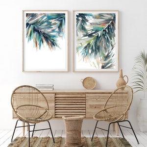 Puede incluir: Dos impresiones enmarcadas en acuarela con hojas de palmera abstractas en tonos turquesa, verde y marr&oacute;n. Las impresiones se exhiben sobre un mueble de madera con sillas tejidas y una alfombra, creando una est&eacute;tica costera y bohemia.