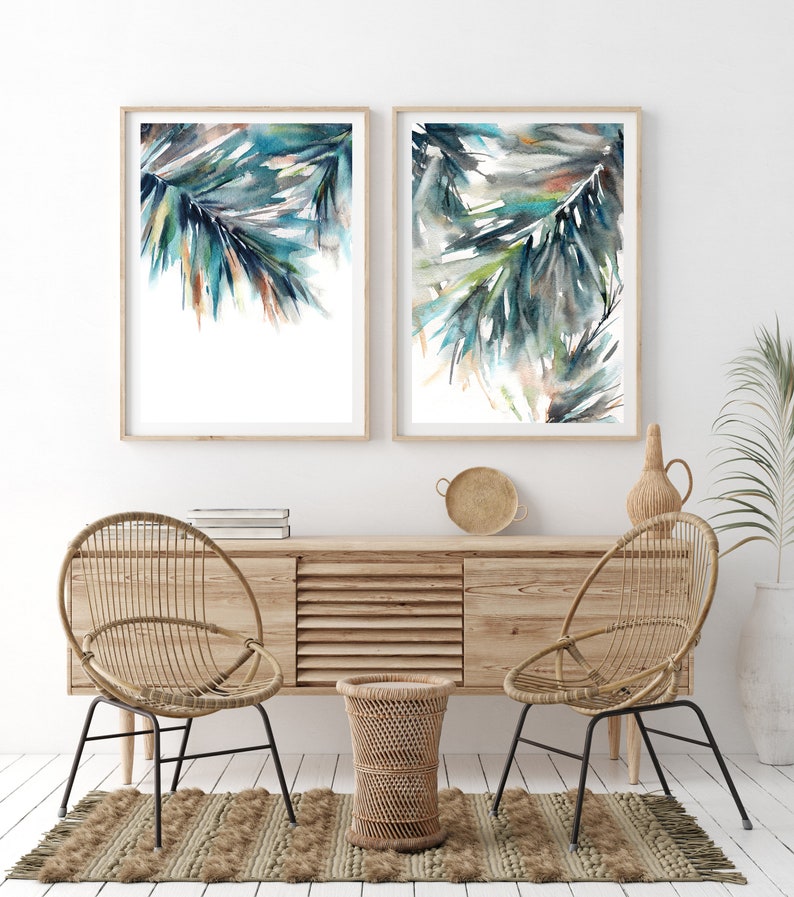 Puede incluir: Dos impresiones enmarcadas en acuarela con hojas de palmera abstractas en tonos turquesa, verde y marr&oacute;n. Las impresiones se exhiben sobre un mueble de madera con sillas tejidas y una alfombra, creando una est&eacute;tica costera y bohemia.