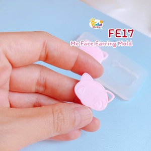 May include: Pink silicone mold for making earrings. The mold features a cute cartoon face with large eyes and a small mouth. The mold is labeled "FE17 Me Face Earring Mold".