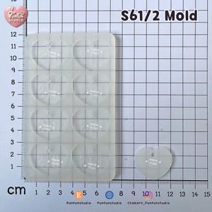 May include: A translucent silicone mold featuring eight heart-shaped cavities, labeled S61/2 Mold. The mold is positioned on a grid mat with centimeter markings. A single detached heart-shaped piece is shown next to the mold, which measures approximately 12 cm in length.
