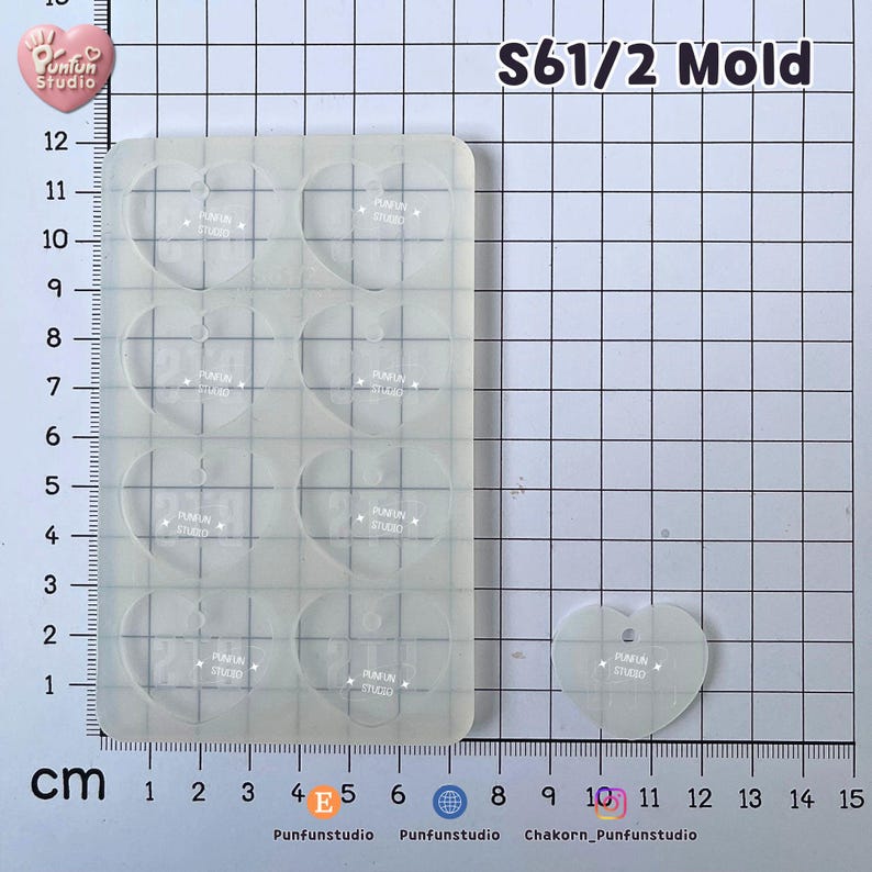 May include: A translucent silicone mold featuring eight heart-shaped cavities, labeled S61/2 Mold. The mold is positioned on a grid mat with centimeter markings. A single detached heart-shaped piece is shown next to the mold, which measures approximately 12 cm in length.
