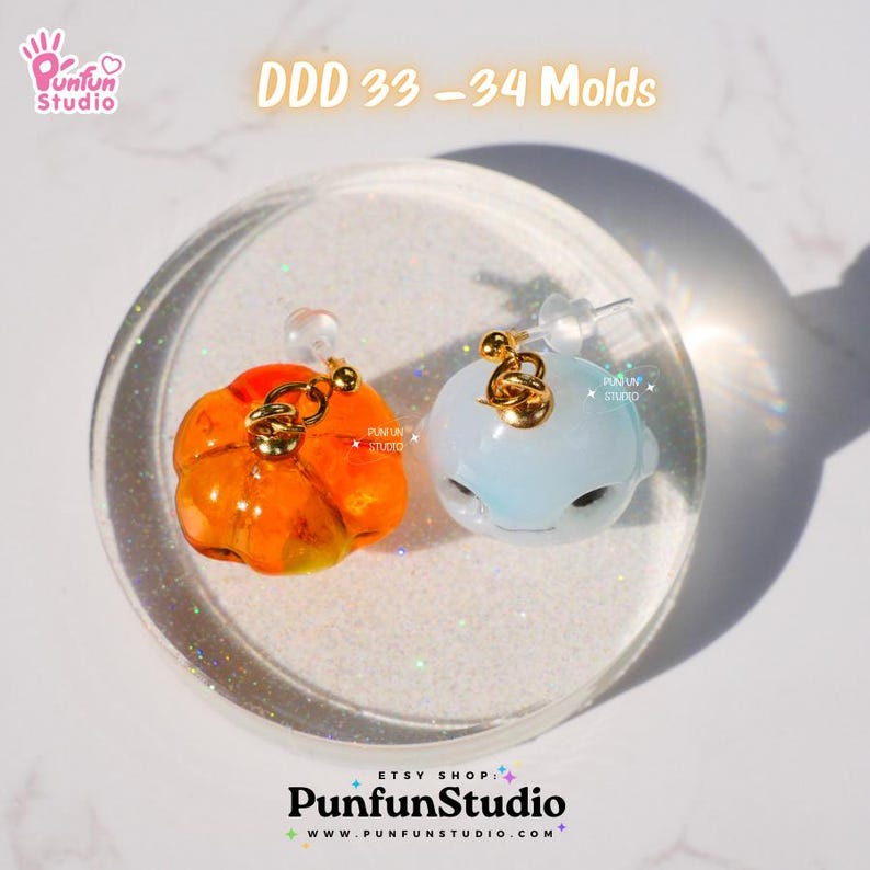 May include: Two resin molds for making earrings. One mold is orange and shaped like a pumpkin. The other mold is light blue and shaped like a whale. The molds are on a white background with glitter.