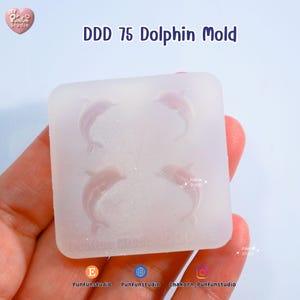 May include: A clear, square mold with four dolphin shapes. The text "DDD 75 Dolphin Mold" is printed at the top. The mold is held in a hand. The Punfun Studio logo is in the top left corner.