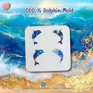 May include: A white square mold with four dolphin designs. Each dolphin is a mix of blue, purple, and pink, with a galaxy-like pattern. The text "DDD 75 Dolphin Mold" is at the top. The background is a watercolor ocean scene.