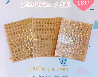 May include: Three sheets of gold letter stickers on a light pink background. Each sheet has a full alphabet of gold letters, 4.5 mm in size. The text "Letter Sticker / Gold LS11" is at the top of the image.