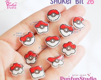 May include: A collection of 10 red and white shaker bits with a pokeball design. The shaker bits are in the shape of a circle, heart, flower, and butterfly. The shaker bits are on a hand.