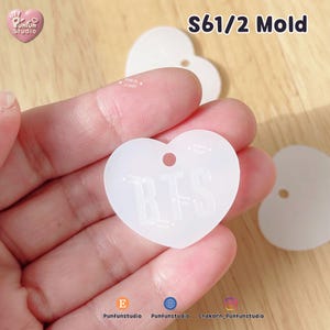 May include: A translucent white heart-shaped silicone mold featuring the embossed letters BTS and a small circular hole at the top. The mold is semi-transparent with a smooth finish, designed for crafting small decorative items or charms.
