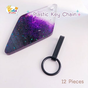 May include: A set of 12 purple and black resin keychains with glitter. Each keychain features a diamond-shaped resin charm with a black plastic key ring. The charms have a gradient of purple and black with iridescent glitter throughout. The text "Plastic Key Chain" is printed on the image.