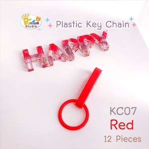 May include: Red plastic key chain with the word "HAPPY" spelled out in clear resin with dried flowers inside. The keychain is labeled "KC07 Red 12 Pieces".