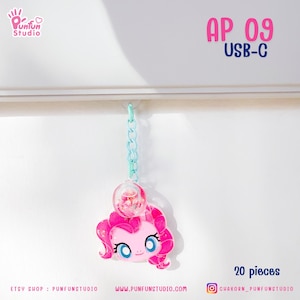 Puede incluir: Encanto de personaje Pinkie Pie con purpurina, en una burbuja transparente con confeti rosa y blanco, colgando de una cadena azul claro. El encanto está etiquetado como "AP 09 USB-C" y "20 piezas".