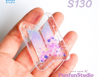 May include: A clear plastic charm shaped like a stylized arrow with a purple and pink gradient and glitter inside. The charm is filled with small, colorful beads and glitter. The charm is labeled "S130".