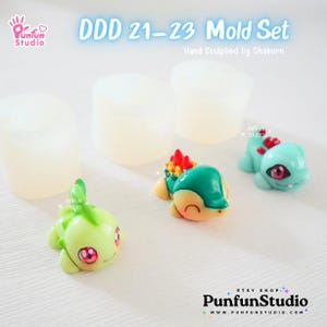May include: A set of three silicone molds for making small figurines. The molds are clear and feature three different designs: a green and red Pokemon character, a blue and yellow Pokemon character, and a green Pokemon character. The molds are labeled "DDD 21-23 Mold Set" and "Hand Sculpted by Chakorn".