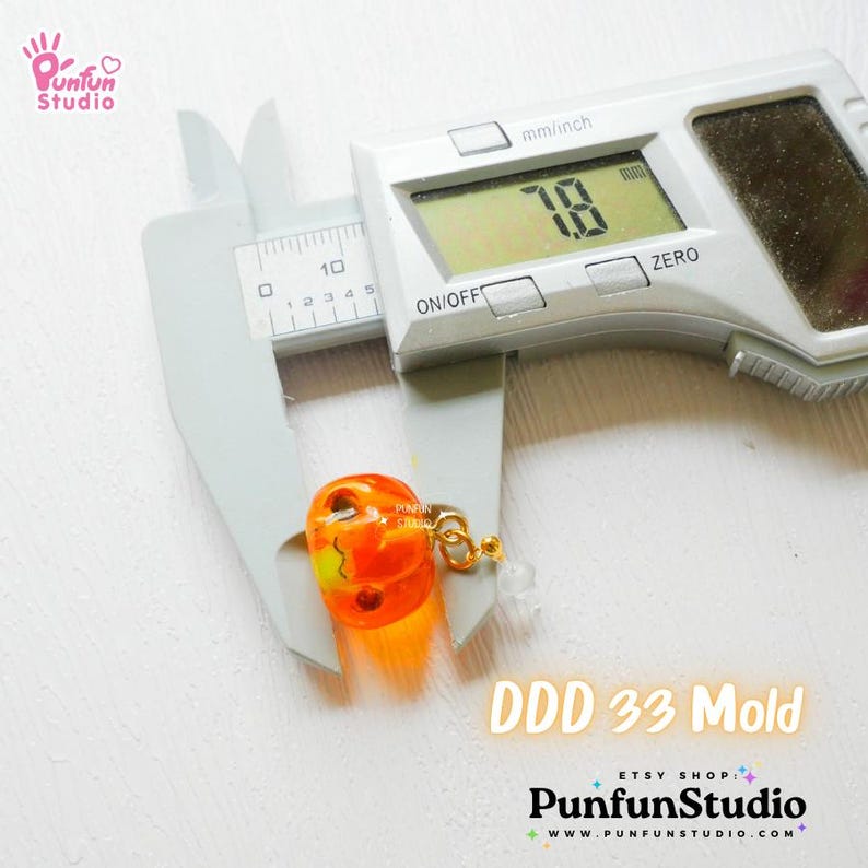 May include: A close-up of a small orange pumpkin-shaped resin mold with a gold jump ring. The mold is being measured with a digital caliper, which reads 7.8 mm. The text "DDD 33 Mold" is visible below the mold.