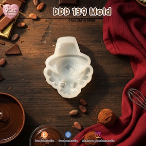 K&ouml;nnte beinhalten: Eine wei&szlig;e Silikonform mit der Aufschrift DDD 139 Mold Chocolate Mold, die ein vertieftes Design einer Figur mit einem breitkrempigen Hut und Fl&uuml;geln zeigt. Die Form hat eine glatte, flexible Oberfl&auml;che zur Herstellung von Schokoladenfiguren.