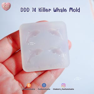 May include: A clear silicone mold with four killer whale designs. The text "DDD 74 Killer Whale Mold" is printed at the top. The mold is held in a hand.