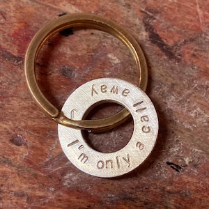 Può includere: Un portachiavi in ​​ottone con un ciondolo in argento che recita "Sono solo una chiamata" e "KEME".