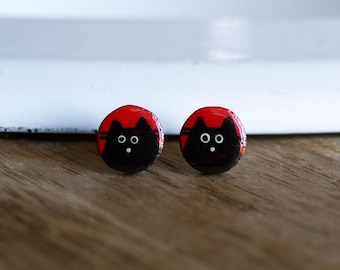 Könnte beinhalten: Ein Paar schwarze Katzen-Ohrstecker mit weißen Augen und rotem Hintergrund.