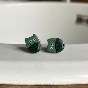 Op de afbeelding: Een paar groene oorbellen met een uil-ontwerp. De uilen zijn geschilderd met zwarte details en witte ogen.
