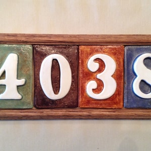 May include: A wooden framed house number sign with four ceramic tiles, each with a different color and a white number. The numbers are 4038.